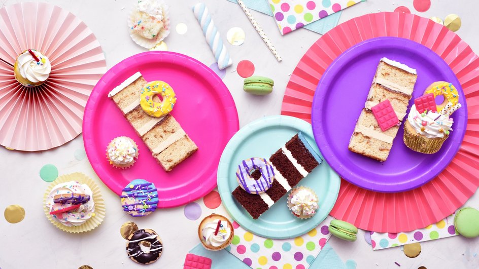 Куски торта, пирожные и пончики лежат на ярких цветных тарелках.