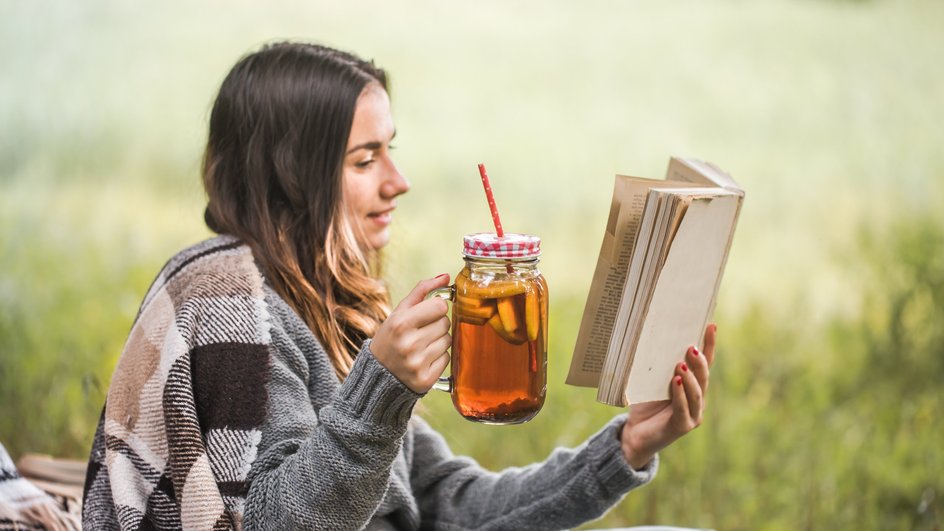 Молодая женщина пьет чай и читает книгу ранним вечером на даче Молодая женщина пьет чай и читает книгу ранним вечером на даче
