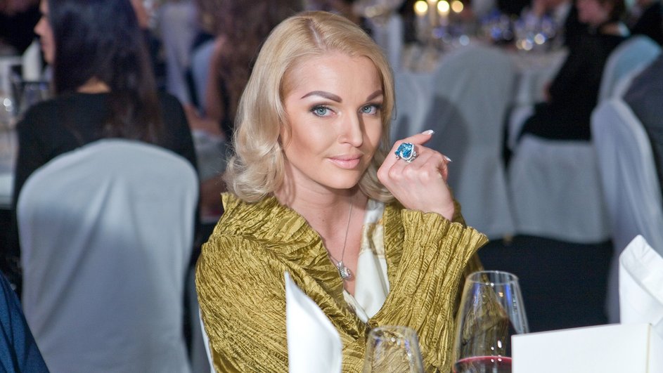 Анастасия Волочкова в золотом платье на фоне столов
