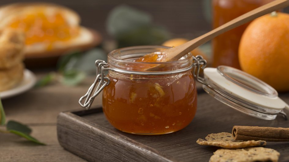 Варенье из тыквы с курагой в открытой банке с крышкой с деревянной ложкой стоит на деревянной подставке рядом с палочкой корицы и парой печений на столе Варенье из тыквы с курагой в открытой банке с крышкой с деревянной ложкой стоит на деревянной подставке рядом с палочкой корицы и парой печений на столе