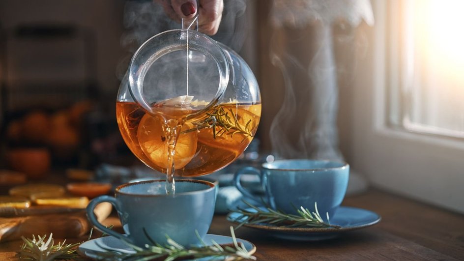 Из прозрачного чайника разливается чай в голубые чашки 