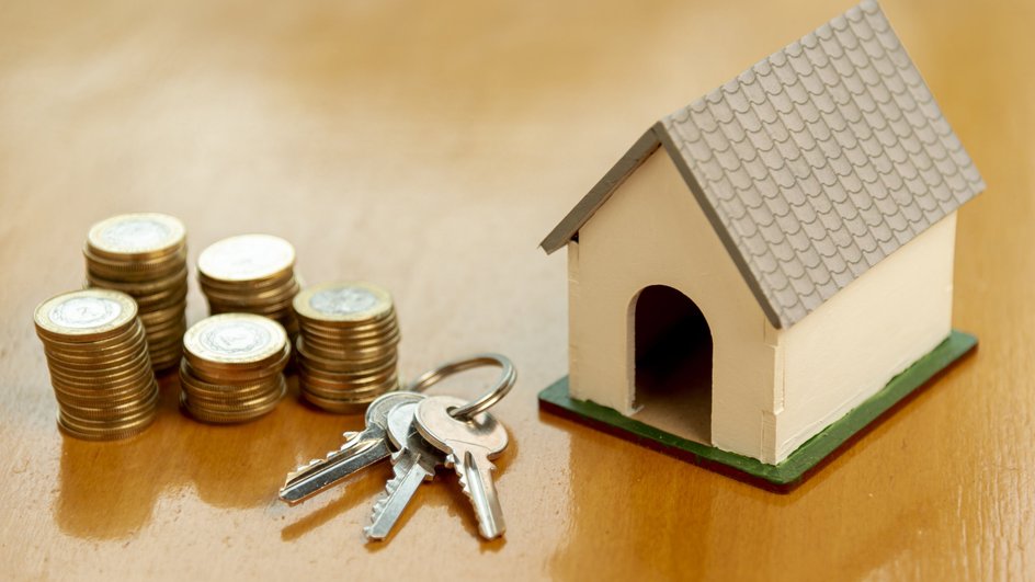 Деревянный макет дома с ключами и монетами стоит на столе