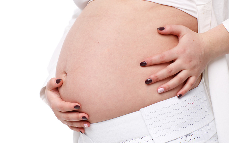 Ребенок в животе беременной и бандаж. На животе у беременной светлая кожа. Повязка живота во время беременности.