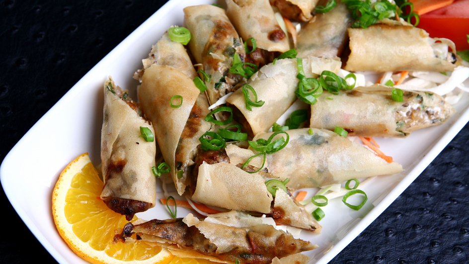 Обжаренные рулетики из лаваша с мясной начинкой, украшенные зеленым луком, лежат на тарелке