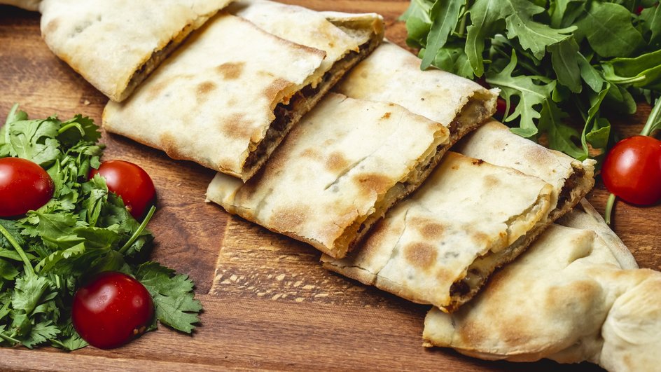 Хрустящие рулеты из лаваша с курицей лежат на столе рядом с помидорами и зеленью