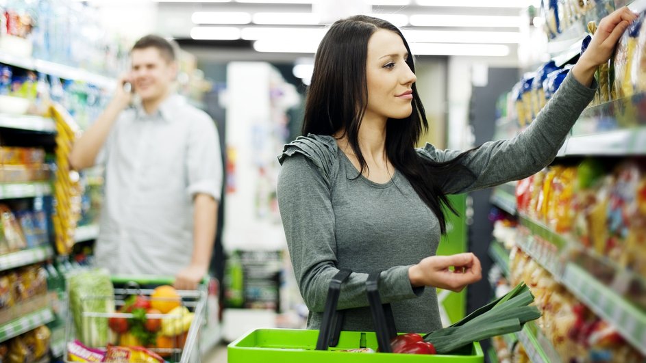 Девушка выбирает жареные самачки подсолнуха в магазине продуктов и берет с полки одну из пачек Девушка выбирает жареные самачки подсолнуха в магазине продуктов и берет с полки одну из пачек