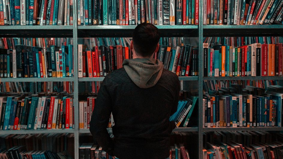 Человек стоит перед шкафом с книгами Человек стоит перед шкафом с книгами