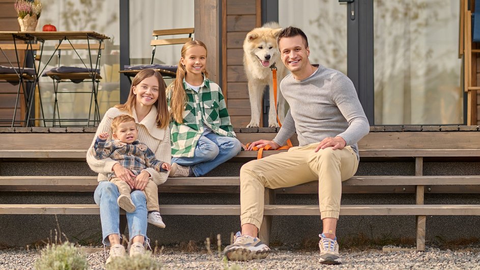 Муж, жена, двое детей и собака сидят на крыльце загородного дома