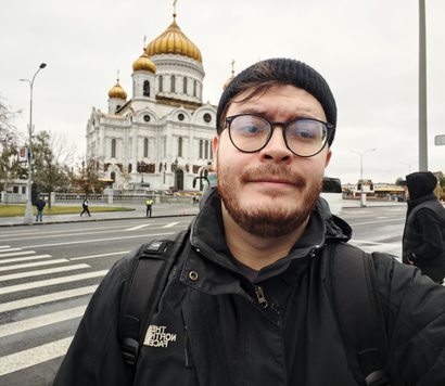 Молодой человек в черной куртке, черной шапке и очках делает селфи на фоне Храма Христа Спасителя