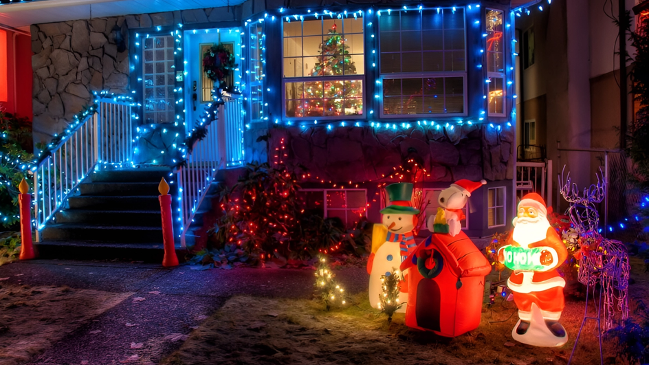 Наряженный гирляндой синего цвета дом с крыльцом, у крыльца стоят статуэтки: снеговик, домик и Дед Мороз.