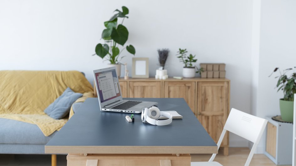 В гостиной на столе стоит ноутбук, рядом белый стул на фоне дивана и комода