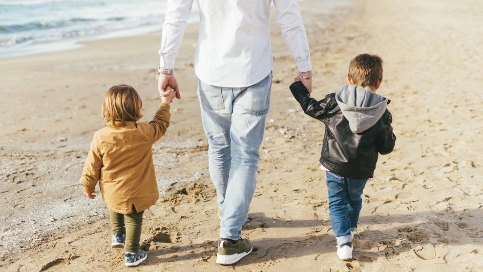 Отец-Стрелец идет с детьми за руку по пляжу 