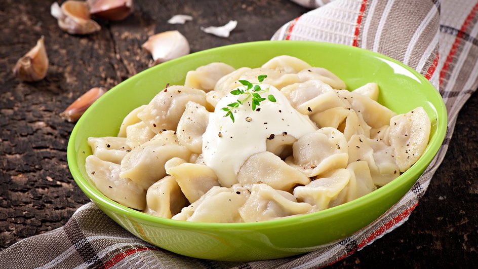 Пельмени с куриным фаршем и сыром, украшенные сметаной, в зеленой тарелке Пельмени с куриным фаршем и сыром, украшенные сметаной, в зеленой тарелке