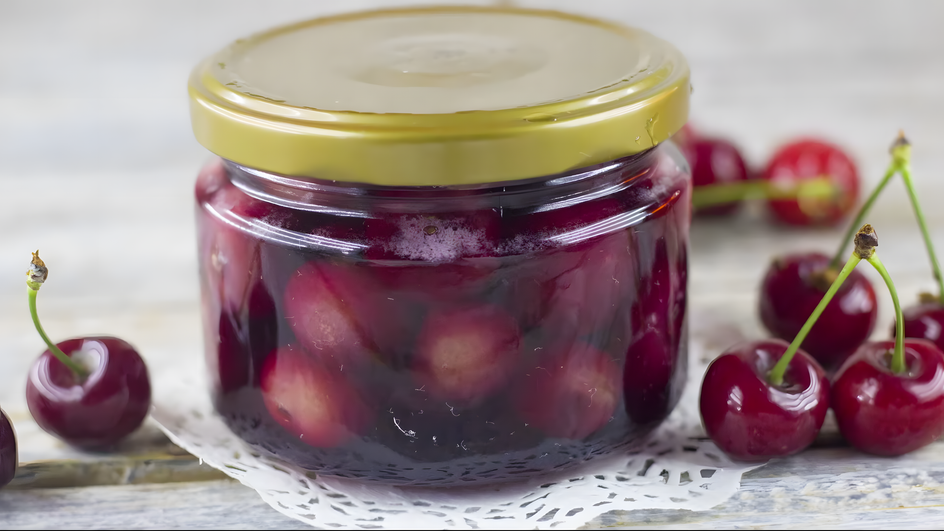 Банка варенья из красной черешни с косточками стоит на столе рядом с черешней Банка варенья из красной черешни с косточками стоит на столе рядом с черешней