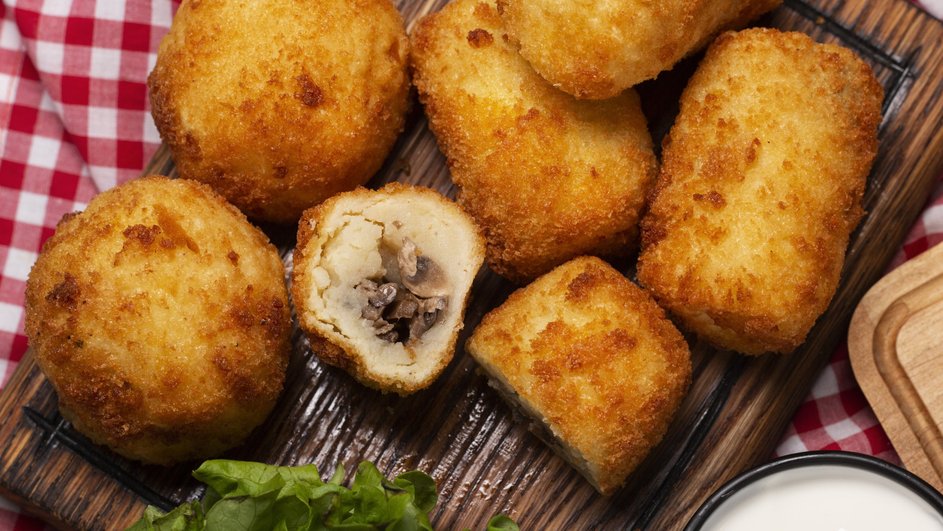 Картофельные котлеты с начинкой из маслят, поданные на деревянной доске с листом салата и соусом