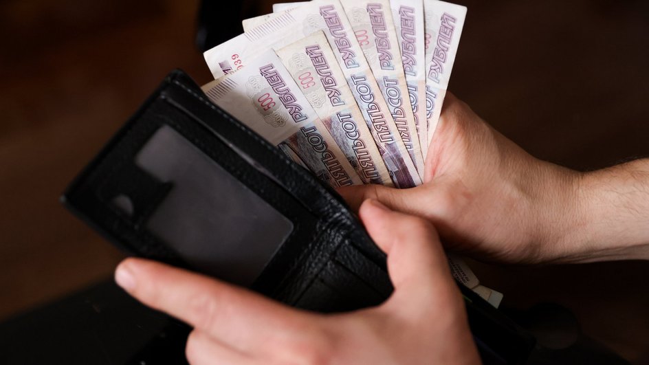 Человек достает из черного кошелька купюры номиналом 500 российских рублей Человек достает из черного кошелька купюры номиналом 500 российских рублей