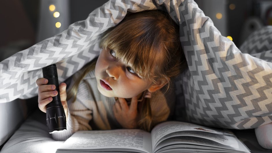 Ребенок читает книгу под одеялом с фонариком