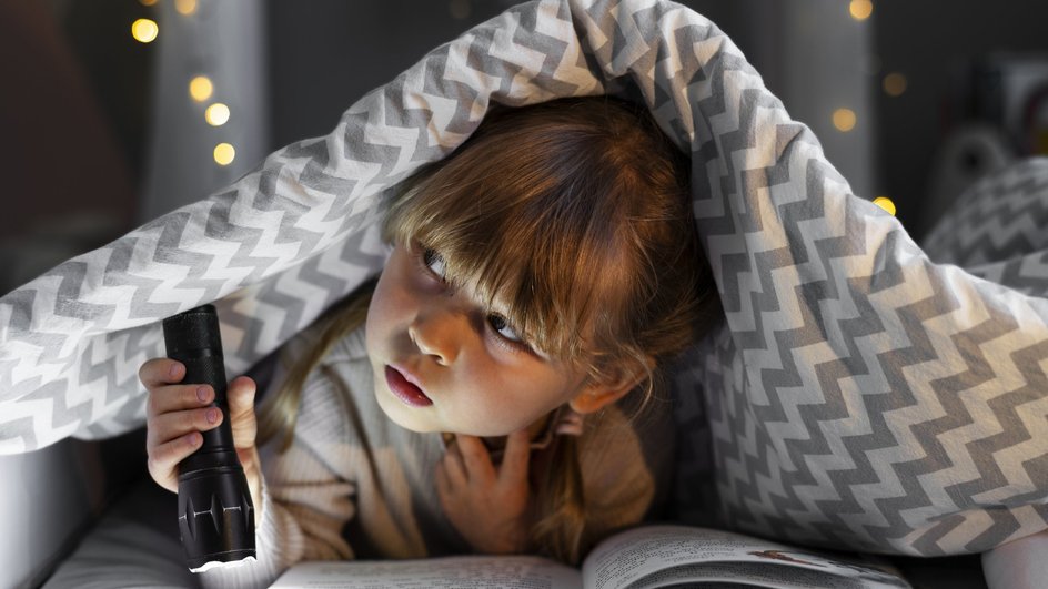 девочка читает с фонариком под одеялом