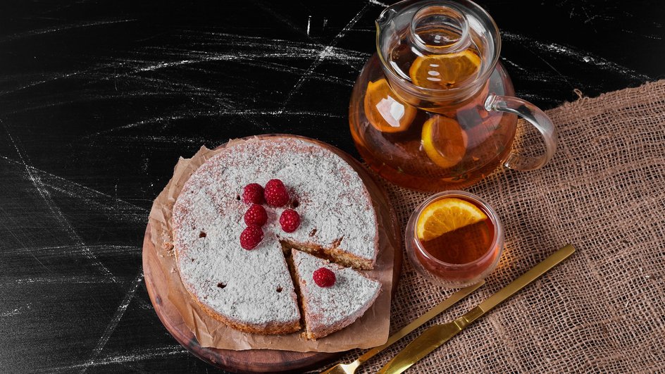 Вкусный пирог с вишневым вареньем без дрожжей лежит на доске рядом с чашкой чая и чайником