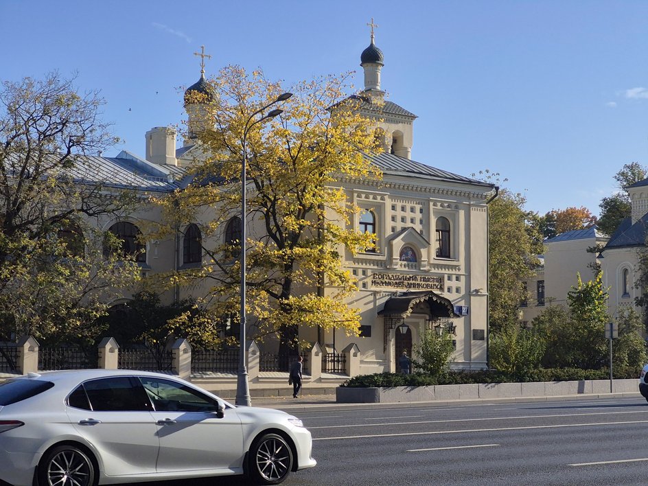 Белая машина на дороге перед бежевым зданием церкви