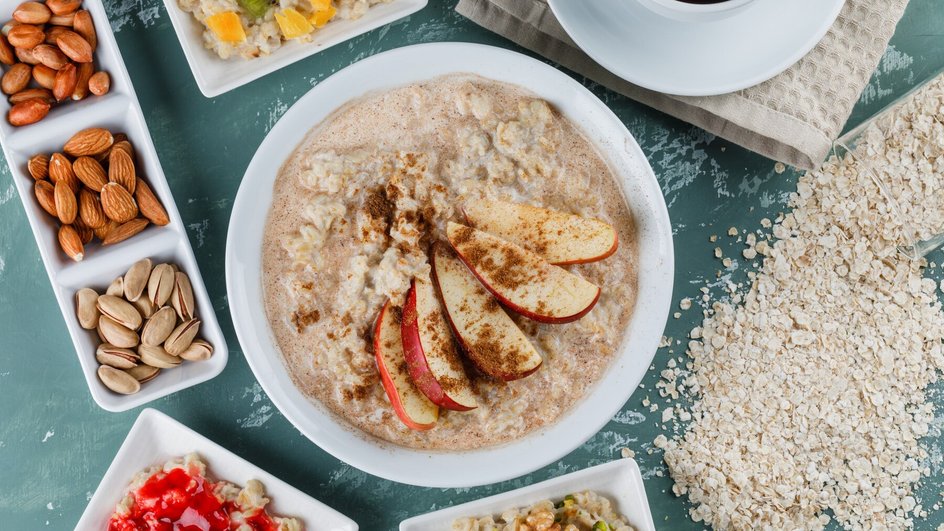 Тарелка овсянки с яблоками, корицей и орехами на фоне различных ингредиентов: орехов, фруктов и соусов.