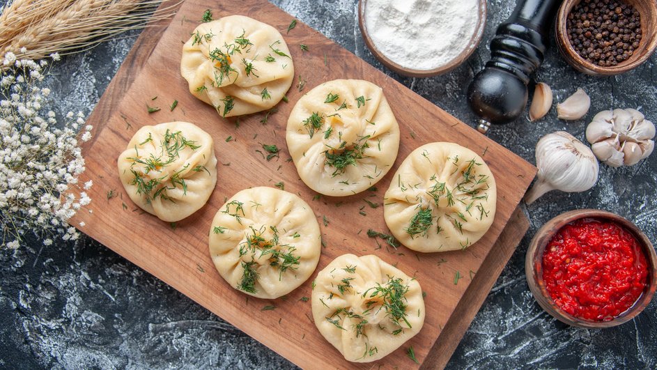 Домашние хинкали с мясом лежат на доске рядом с ингредиентами
