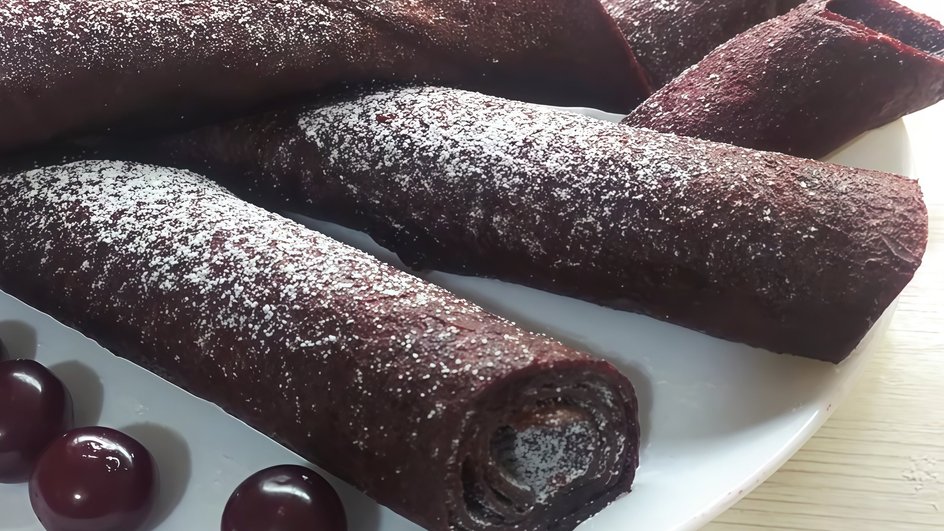 Домашняя пастила из замороженной вишни в электросушилке, посыпанная сахарной пудрой, лежит на белой тарелке с ягодами вишни Домашняя пастила из замороженной вишни в электросушилке, посыпанная сахарной пудрой, лежит на белой тарелке с ягодами вишни