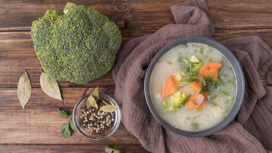 Тарелка супа с брокколи, помидорами и курицей стоит на столе рядом с ингредиентами