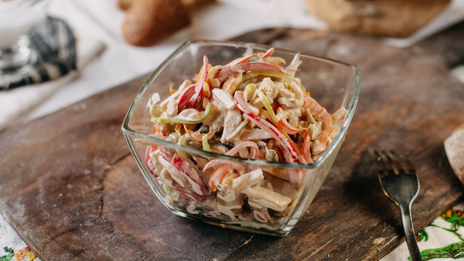Салат с корейской морковью, фасолью и грибами лежит в маленькой салатнице на деревянной доске