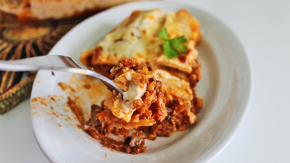 Каннеллони с мясным фаршем и томатным соусом на вилке и в тарелке Каннеллони с мясным фаршем и томатным соусом на вилке и в тарелке