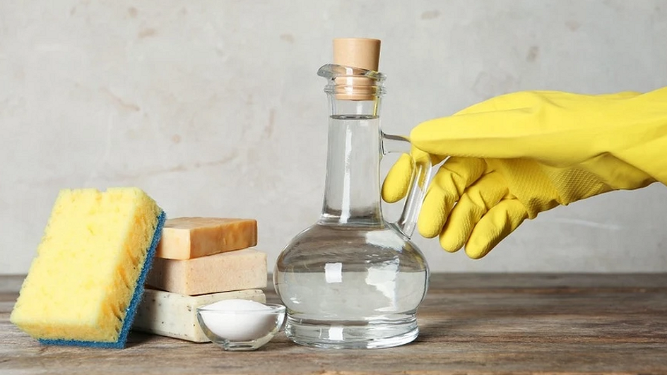 Рука в желтой перчатке держит прозрачный кувшин на фоне губок для посуды 