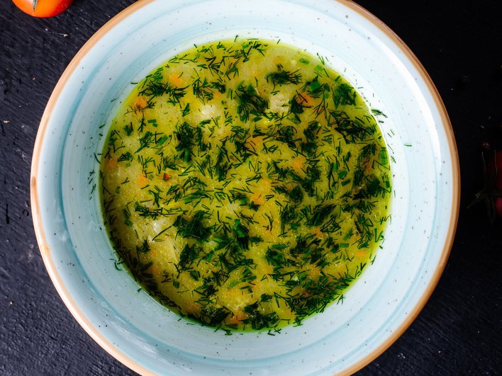 Зеленые щи из свежего щавеля с курицей, украшенные зеленью, в глубокой тарелке стоят на столе Зеленые щи из свежего щавеля с курицей, украшенные зеленью, в глубокой тарелке стоят на столе