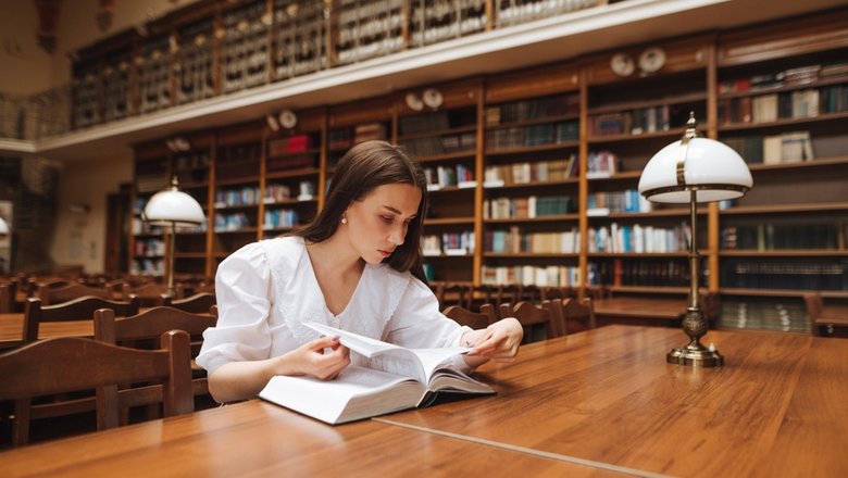 Девушка в библиотеке читает книгу.