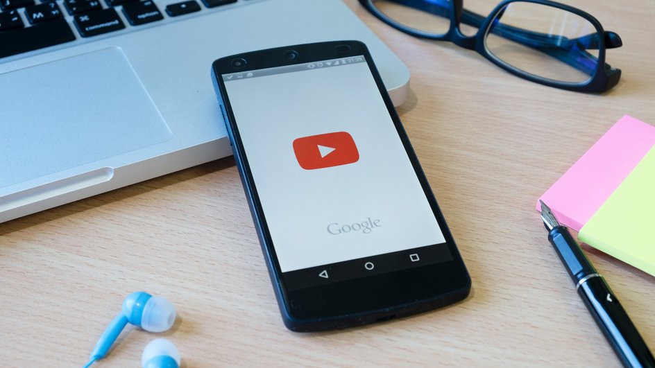 Телефон на столе с запущенным приложением YouTube Телефон на столе с запущенным приложением YouTube