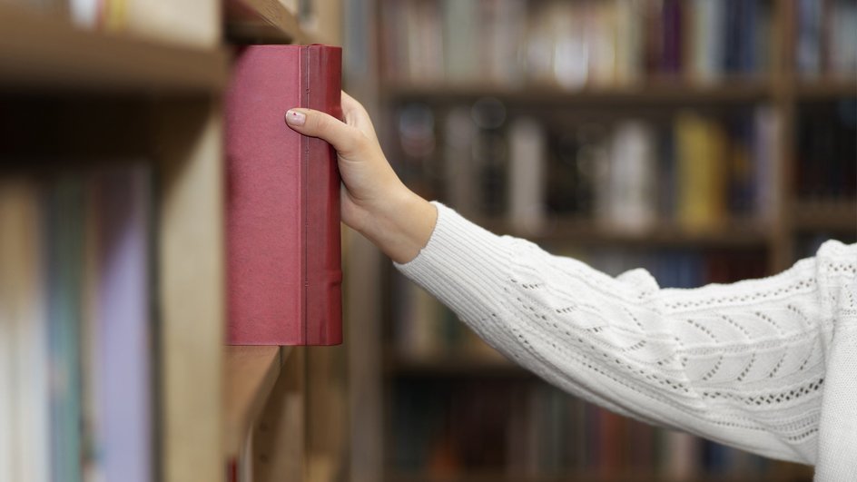Девушка берет с полки книгу по борьбе с прокрастинацией Девушка берет с полки книгу по борьбе с прокрастинацией