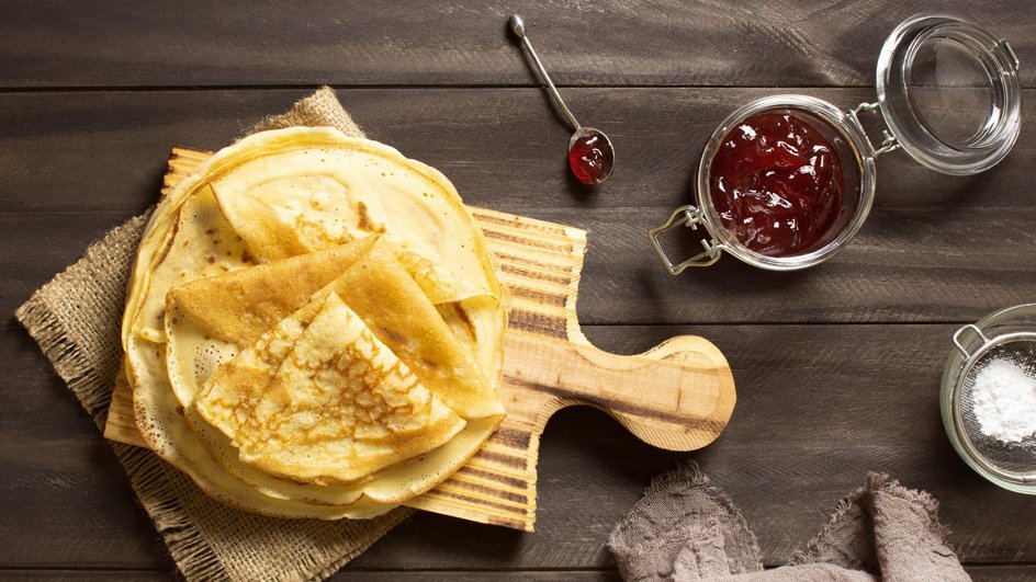 Блины на кокосовом молоке с яйцами лежат на доске рядом с вареньем Блины на кокосовом молоке с яйцами лежат на доске рядом с вареньем