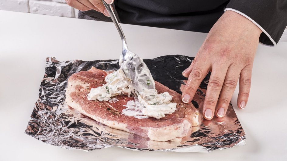 Женщина накладывает соус на мясо, лежащее на фольге Женщина накладывает соус на мясо, лежащее на фольге
