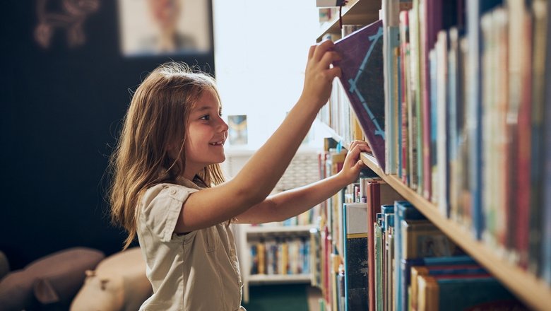 Девочка выбирает книгу в библиотеке.