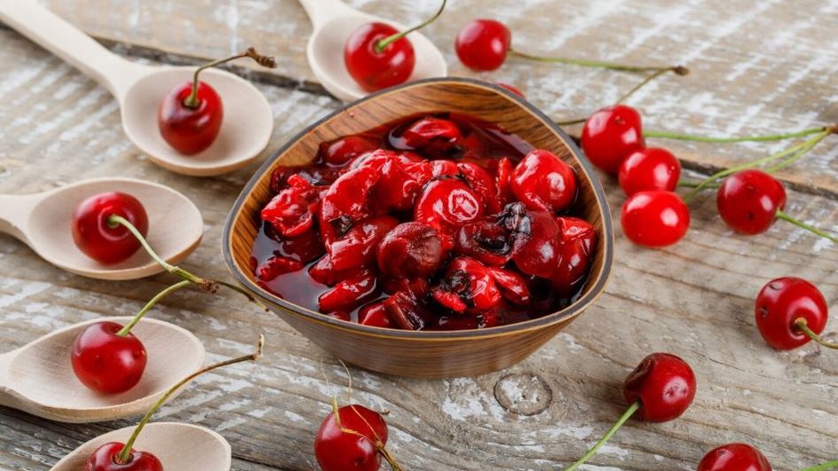Жареное вишневое варенье, окруженное ложками и свежими ягодами Жареное вишневое варенье, окруженное ложками и свежими ягодами