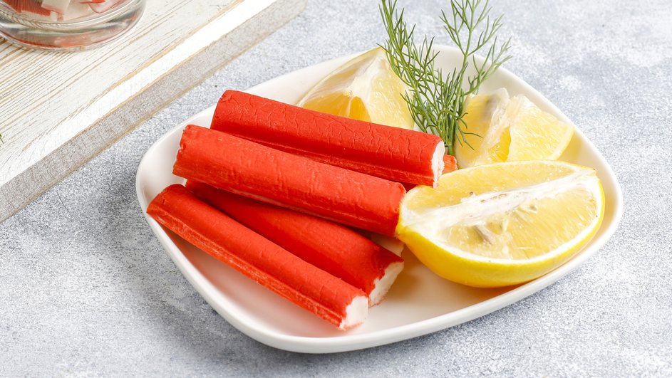 Крабовые палочки лежат на тарелке рядом с лимоном Крабовые палочки лежат на тарелке рядом с лимоном