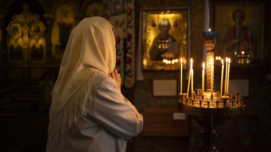 Женщина в белом платке молится перед иконой в православном храме