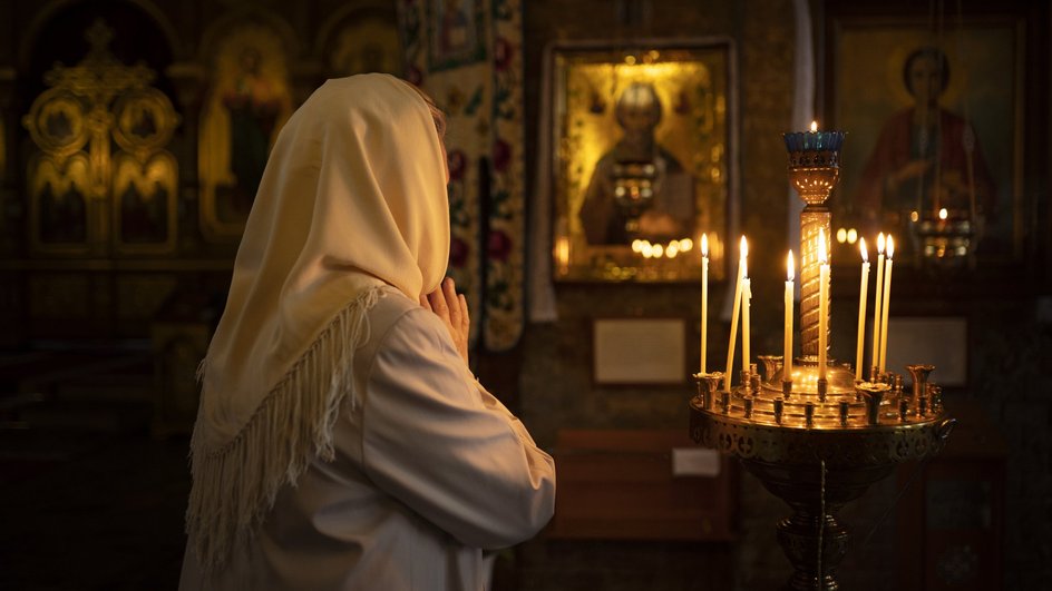 Женщина молится в церкви перед иконой с горящими свечами 