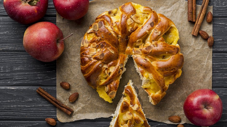 Шарлотка с манкой и яблоками лежит на бумаге для выпекания рядом с ингредиентами