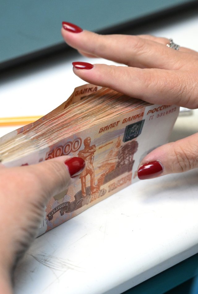 Сотрудница банка пересчитывает купюры номиналом в пять тысяч рублей