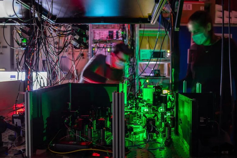 Ученые запечатлены с одним из трех узлов в сети квантовых вычислений, в которой используются зеркала, фильтры и лазеры для направления электронов в синтетический алмаз. Фото: Marieke de Lorijn / QuTech