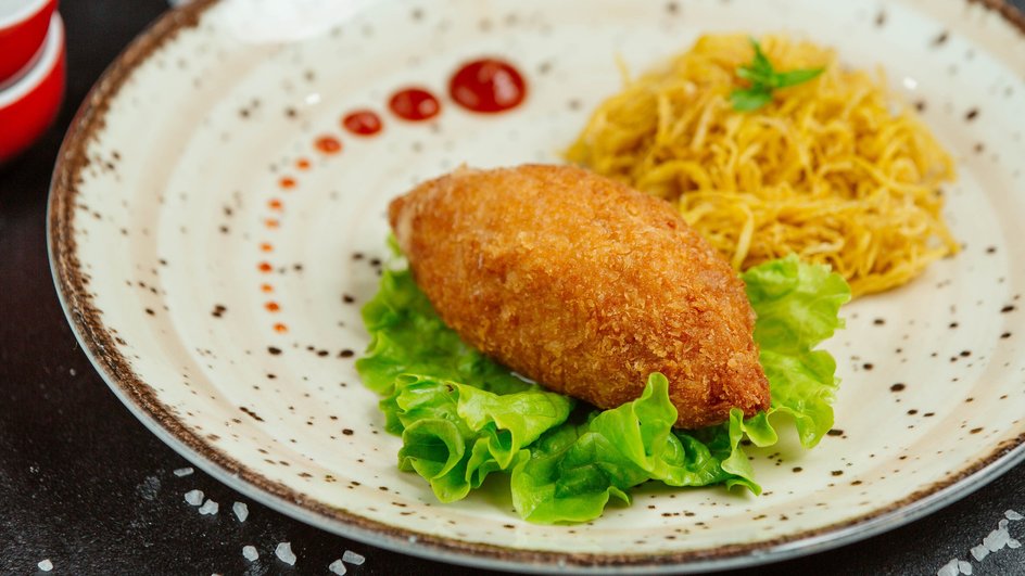 Жареная куриная котлета по-киевски со сливочным маслом лежит на тарелке со пагетти на листе салата Жареная куриная котлета по-киевски со сливочным маслом лежит на тарелке со пагетти на листе салата