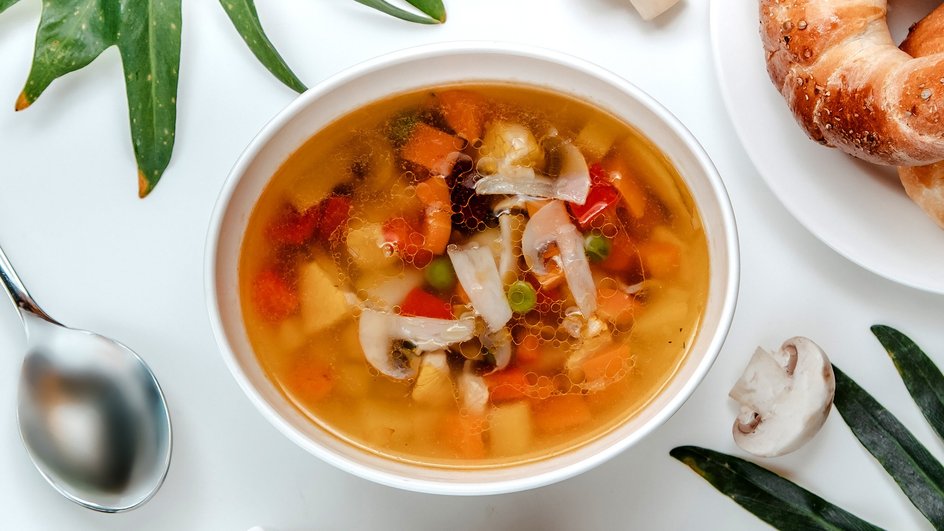 Простой постный суп с шампиньонами и картофелем в белой тарелке на белом столе рядом с ингридиентами