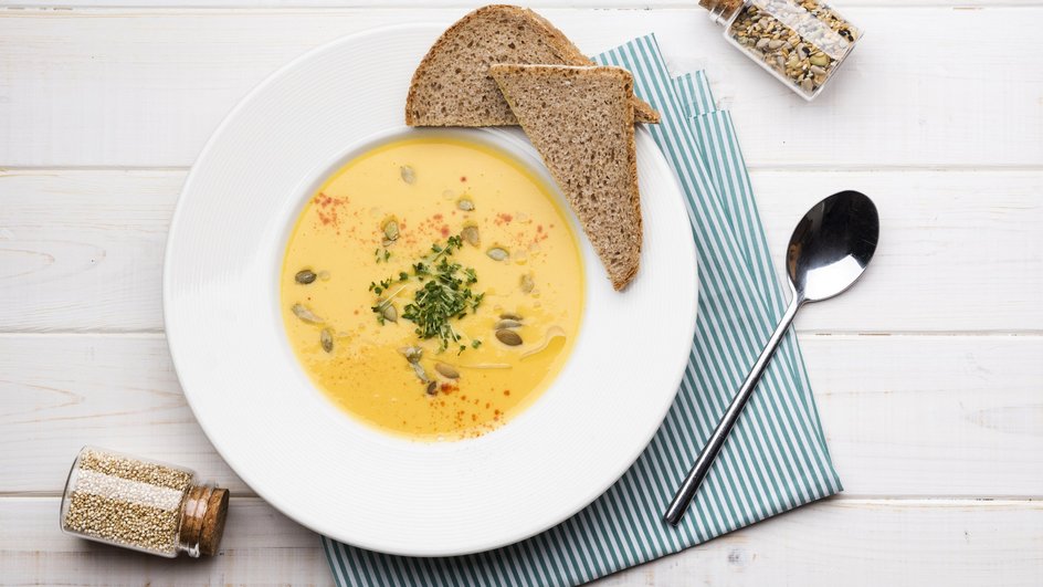 Тарелка сырного супа-пюре без мяса стоит на столе с кусочками хлеба