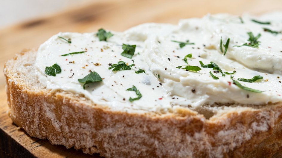 Ломтик хлеба с творожным сыром, посыпанный зеленью и молотым черным перцем на деревянной тарелке