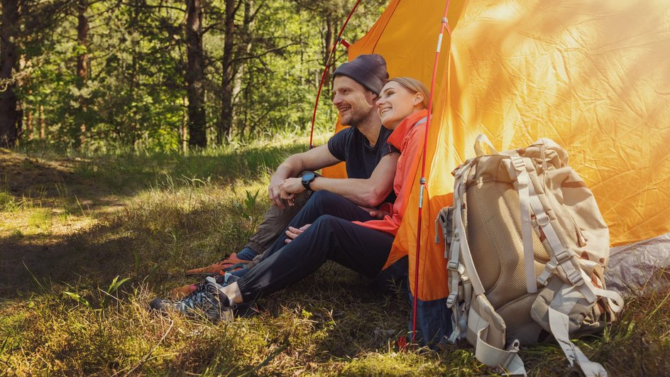 Парень с девушкой сидят в оранжевой палатке в лесу